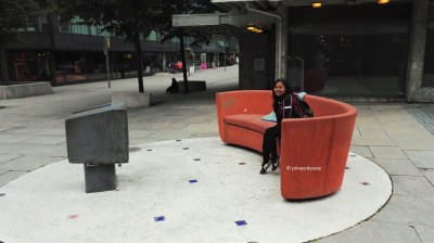 In the middle of the street is an orange cemented sofa and a real TV!
